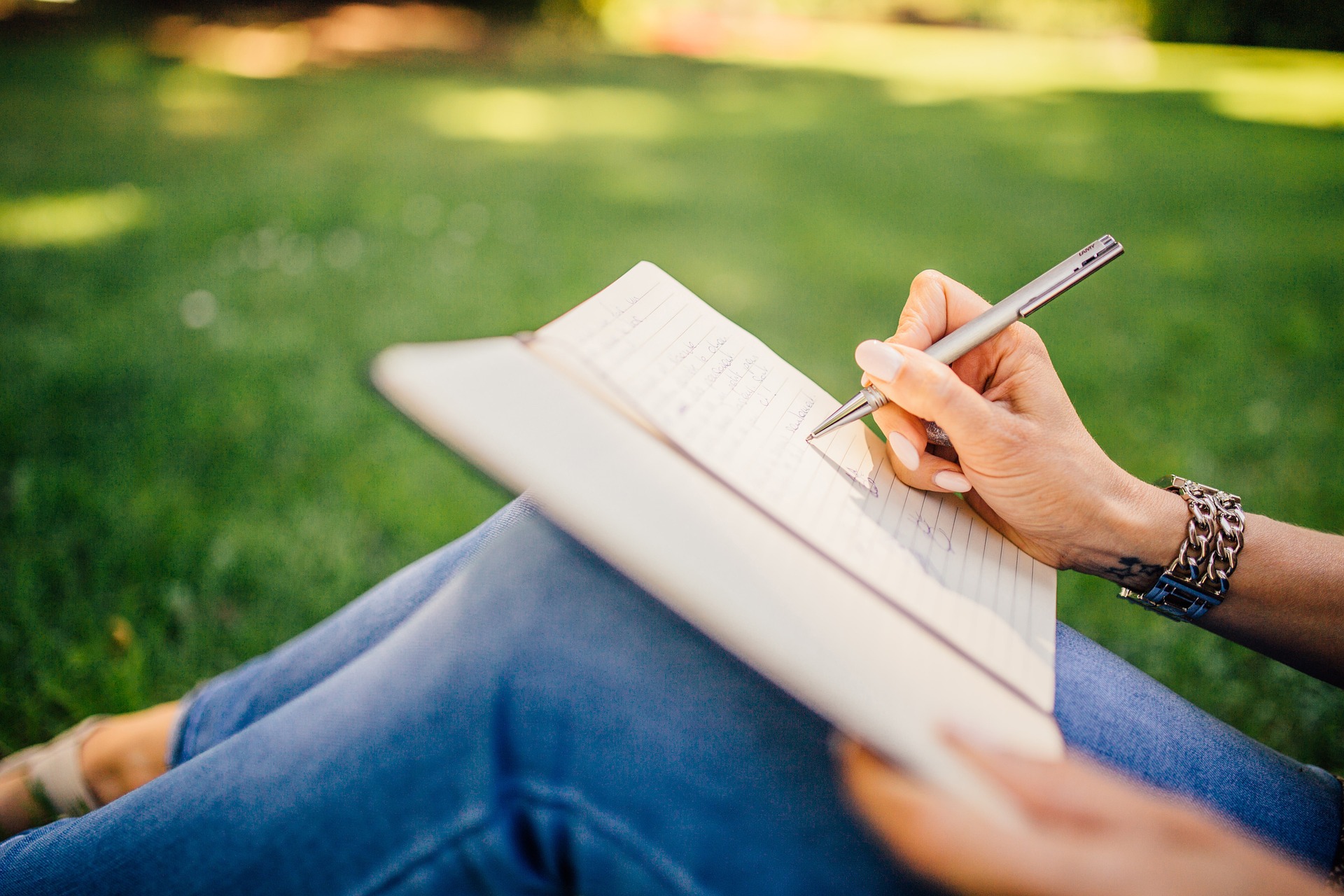 A person sitting in a field of grass, writing in a notebook